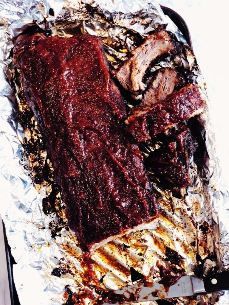 Rack of ribs in a baking sheet covered in sauce