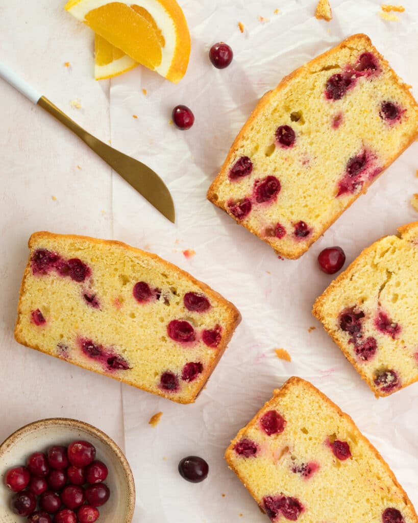 orange and cranberry pound cake slices laid out with a knife and fresh cranberries